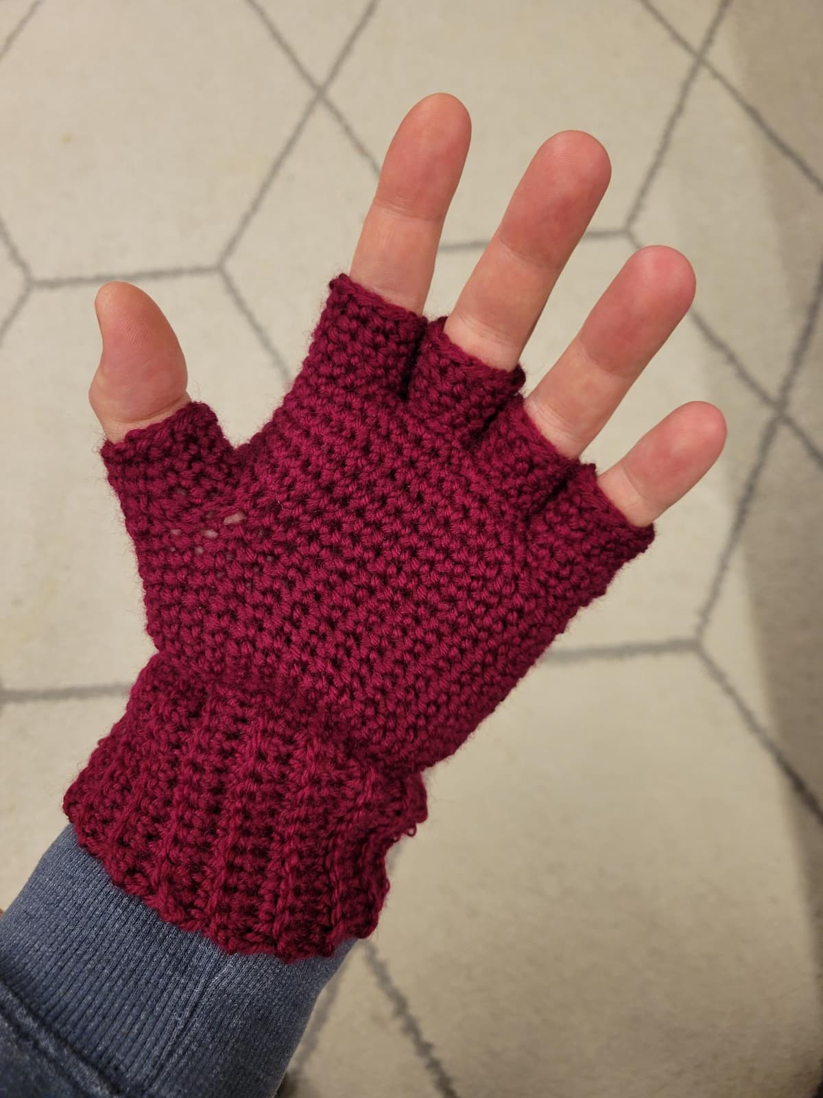 Crocheted fingerless glove worn on a left hand